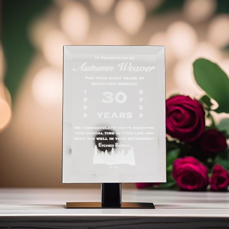 Puede incluir: Placa de vidrio transparente con texto grabado, incluyendo "Autumn Weaver" y "30 YEARS". Montada sobre un soporte negro y dorado. Fondo borroso con rosas rojas. Un regalo conmemorativo.