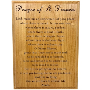 May include: Wooden plaque with the text "Prayer of St. Francis" in elegant script. The prayer is printed in a classic font, set against a light wood grain background. A religious item for home decor.