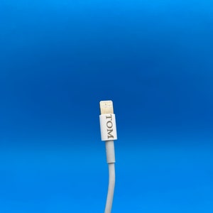May include: White iPhone charging cable with a white connector and the word "TOM" printed on the connector.
