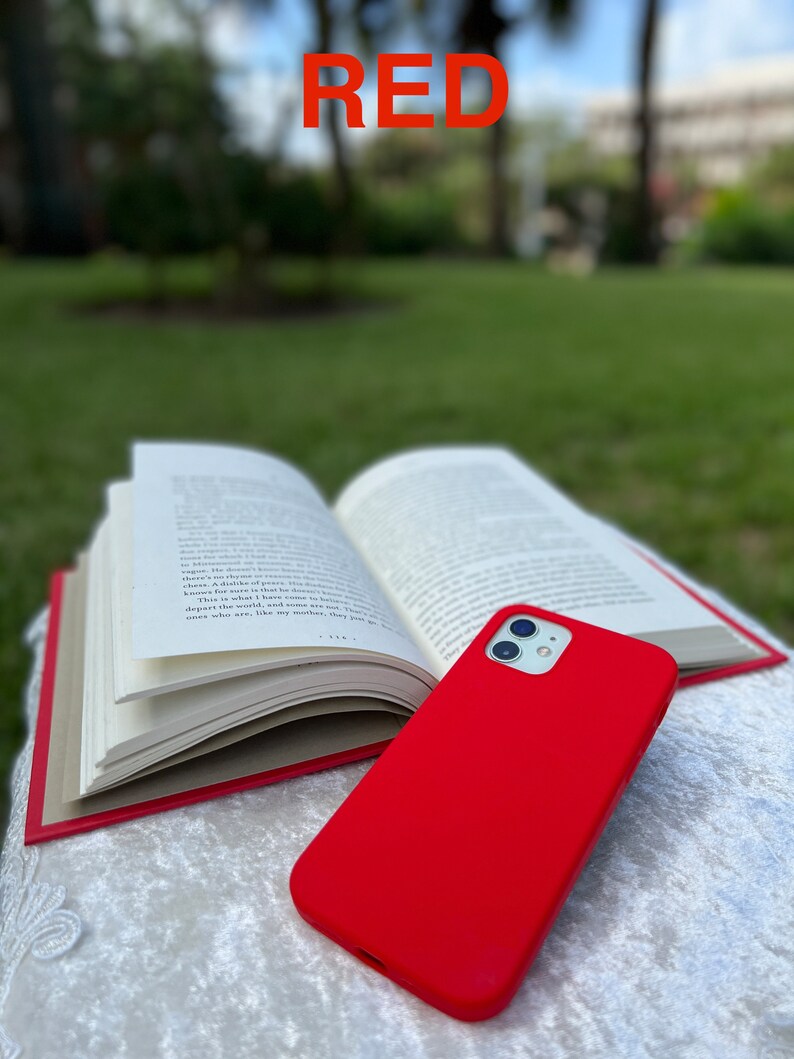 May include: A bright red phone case for an iPhone. The case is made of a soft, flexible material and has a smooth finish. The case is lying on top of a book.