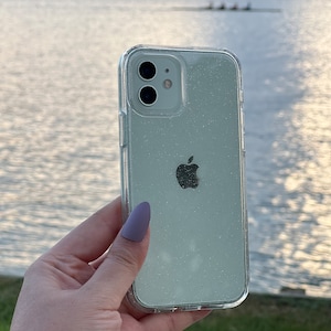 Op de afbeelding: Een transparante telefoonhoes met een glinsterend, lichtgroen glitterontwerp. De hoes heeft een verhoogde camerabult en een duidelijk Apple-logo.
