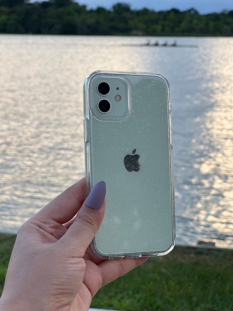 Op de afbeelding: Een transparante telefoonhoes met een glinsterend, lichtgroen glitterontwerp. De hoes heeft een verhoogde camerabult en een duidelijk Apple-logo.