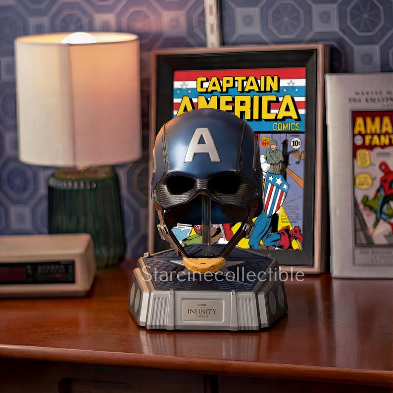 May include: A blue Captain America helmet replica with a large white "A" on the front, displayed on a gray base. The base has the word "INFINITY" on it. A framed Captain America comic book is in the background.