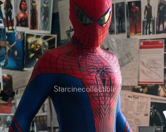 May include: A red and blue Spider-Man costume with a web pattern and a spider emblem on the chest. The mask has yellow lenses. The costume is worn by a person. The background has posters and drawings.