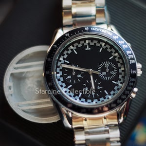 May include: A silver-toned wristwatch with a black face and a checkered pattern around the dial. The watch features multiple sub-dials and a tachymeter scale. The brand name "Starcine Collectible" is visible on the watch face.