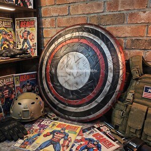 May include: A large, round shield with a distressed metal appearance, featuring concentric rings of red, black, and silver. Comic books with the title "US Agent" and a military helmet are also visible.