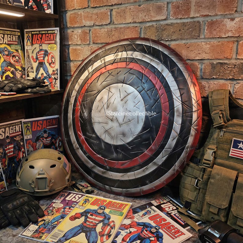 May include: A large, round shield with a distressed metal appearance, featuring concentric rings of red, black, and silver. Comic books with the title "US Agent" and a military helmet are also visible.