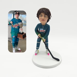 May include: A custom-made figurine of a hockey player wearing a teal jersey with "Mountain Dew" written on it. The figurine is holding a hockey stick and is standing on a white base.