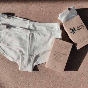 May include: Two pairs of off-white underwear with a small green leaf logo tag on the waistband. Included are two brown cardboard boxes with black text reading good hemp, Why Hemp Fabric, and a size chart with icons for different underwear styles.