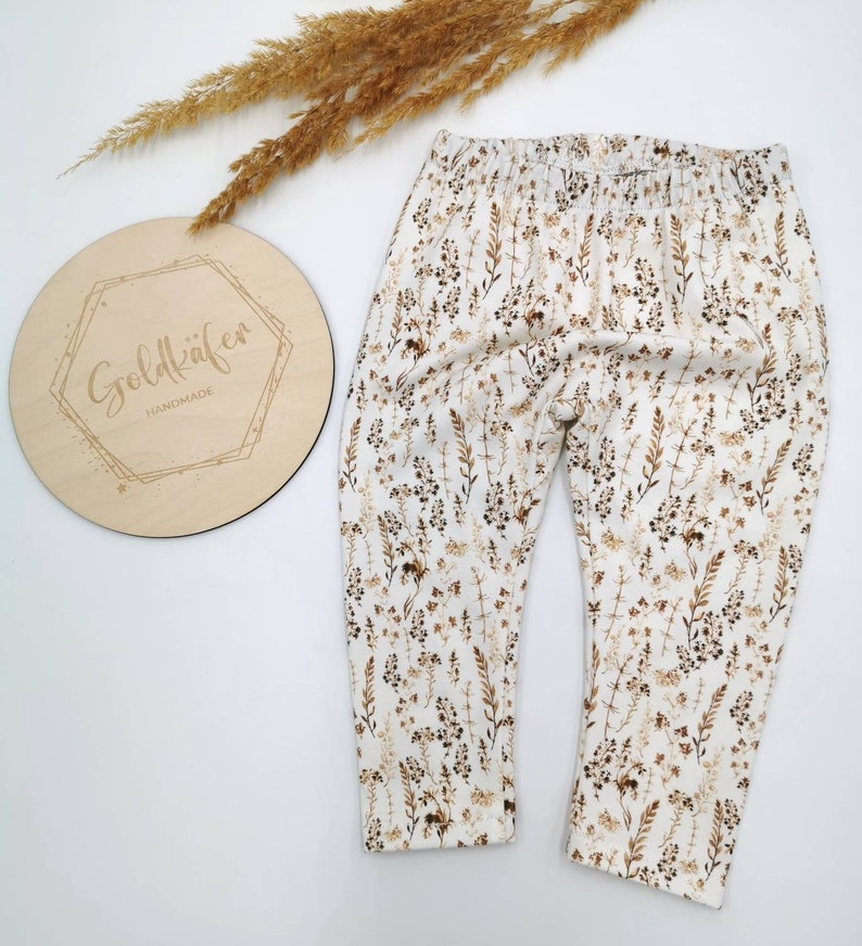 May include: White leggings with a brown floral print. The leggings have an elastic waistband.