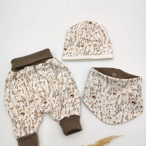 May include: A baby outfit set with a brown and white floral print. The set includes a pair of pants, a hat, and a bib.