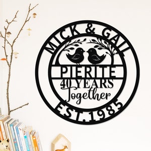 Könnte beinhalten: Schwarzes rundes Schild aus Metall mit dem Text "Mick & Gail Pierite 40 Years Together Est. 1983" und zwei Vögeln auf einem Ast.