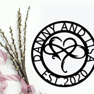 Könnte beinhalten: Schwarzer Metallkreis mit dem Text "Danny and Lisa Est 2020" am Rand. Ein stilisiertes Unendlichkeitszeichen mit einem Herzen in der Mitte.