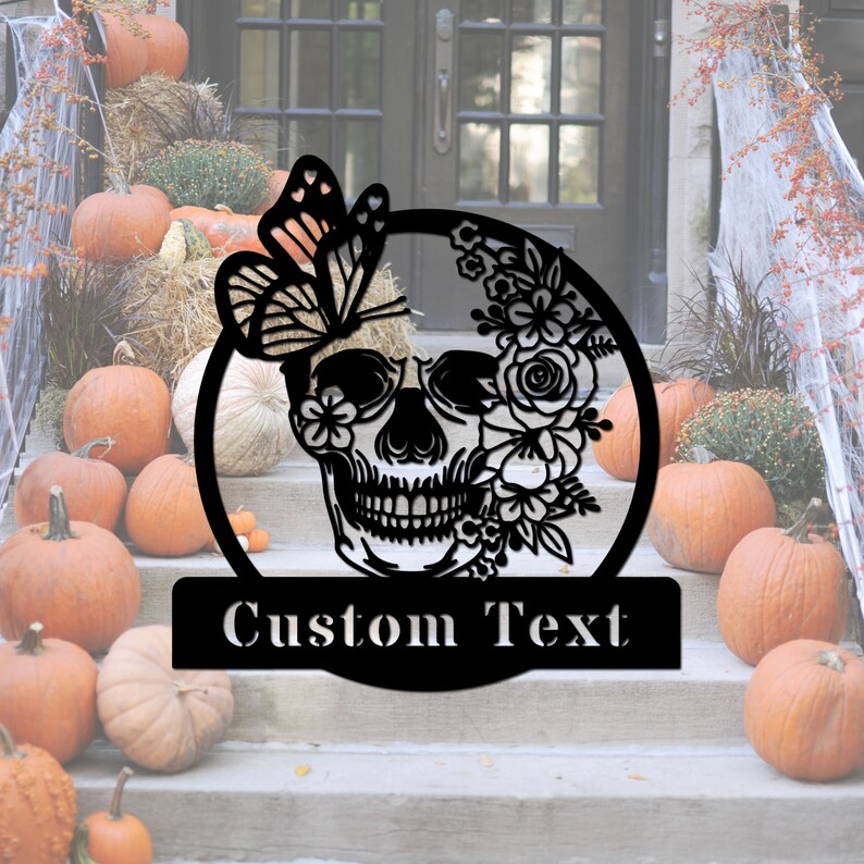 Może przedstawiać: Czarna metalowa dekoracja drzwi na Halloween z czaszką ozdobioną kwiatami i motylem. Czaszka ma kwiatowy wz&oacute;r i motyla z boku. Tekst "Custom Text" znajduje się pod czaszką.
