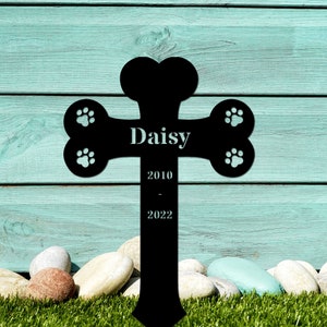 May include: Black metal pet memorial cross shaped like a bone with paw prints and the text "Daisy 2010 - 2022".