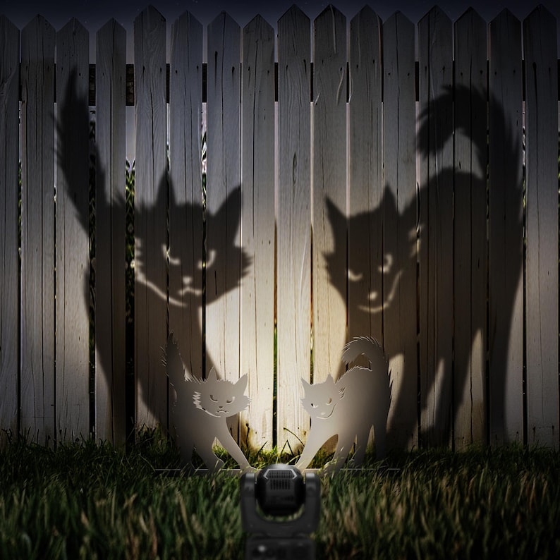 May include: Two white cat silhouettes are illuminated by a flashlight in front of a white picket fence. The shadows of the cats are cast on the fence, creating a spooky Halloween scene.