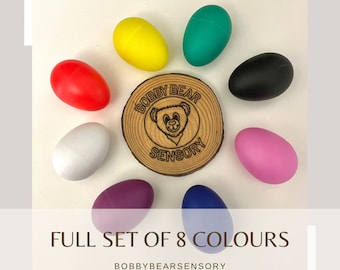 May include: A set of eight colorful egg-shaped sensory toys. The toys are arranged in a circle around a wooden circle with the text "Bobby Bear Sensory".