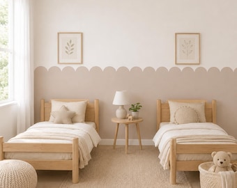 May include: Two light wood twin beds with white bedding, star and round pillows, and a central round side table with a lamp. The wall features a scalloped beige paint design, two framed botanical prints, and a woven rug on the floor.