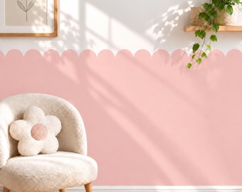 May include: A light pink scalloped wall decal applied to the lower half of a white wall, featuring a smooth curved edge design. The wall is decorated with a framed flower print and a green trailing plant on a wooden shelf above the decal.