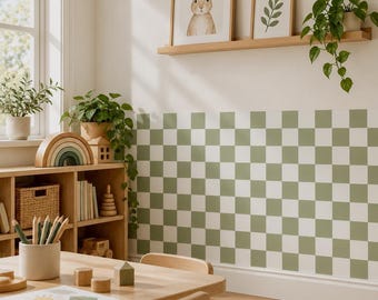 May include: A room interior featuring a wall with a sage green and white checkered pattern. A wooden shelf holds two framed prints of a rabbit and leaves, and a trailing green plant. A wooden bookcase contains books, a rainbow toy, and a basket.