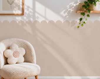 May include: A beige scalloped wall decal border applied to a white wall, featuring a soft curved edge design. The wall is decorated with a framed flower print and a trailing green plant on a wooden shelf, with a cream-colored flower-shaped pillow.