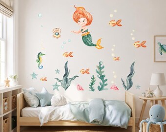 May include: A set of watercolor wall decals featuring a mermaid with orange hair and a green tail, a seahorse, various orange fish, a pearl in a shell, pink seashells, starfish, and green seaweed stalks arranged on a plain white wall.