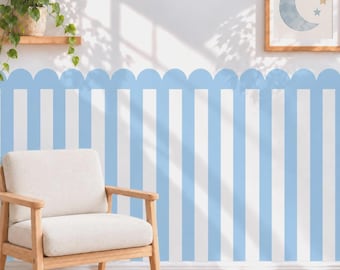May include: A light blue and white vertical striped wallpaper with a scalloped top edge. The wall features a framed print of a crescent moon and stars. A light-colored armchair sits in front of the wall, and a green plant sits on a shelf.