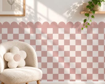 May include: A wall covering featuring a repeating pattern of dusty pink and white squares, finished with a scalloped top edge. The wallpaper is applied to a wall behind a cream-colored textured chair with a flower-shaped pillow on the seat.