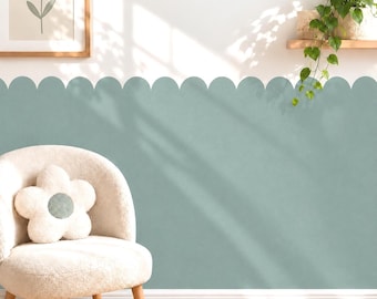 May include: A sage green scalloped wall border decal applied to a white wall. The border features a repeating rounded edge pattern. A cream-colored textured armchair with a flower-shaped pillow sits in front of the wall, near a framed flower print.