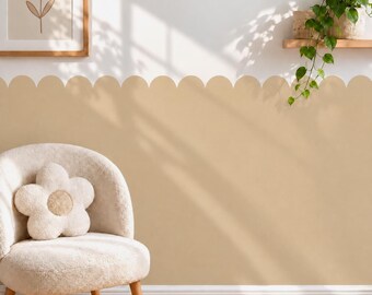 May include: A beige scalloped wall decal applied to the lower half of a white wall, featuring a smooth curved edge design. The wall is decorated with a framed flower line art print and a trailing green plant on a wooden shelf above.