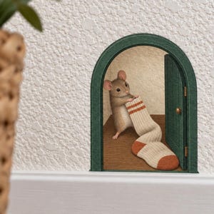 May include: A wall decal featuring an arched green door frame with a small brown mouse standing inside on a wooden floor. The mouse is holding a beige sock with orange stripes and a solid orange toe, positioned as if entering or exiting the room.