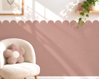 May include: A dusty rose wall decal featuring a scalloped top edge applied to the lower half of a white wall. The wall is decorated with a framed flower print and a wooden shelf holding a green trailing plant above a cream-colored chair.