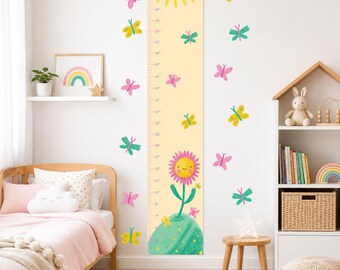May include: A vertical wall growth chart decal featuring a yellow background with a sun at the top, the name Emily, and a smiling flower illustration at the base. The chart includes imperial measurements in inches, surrounded by colorful butterflies.