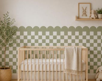 May include: A light-colored wooden crib with a white mattress and a cream-colored throw blanket. The wall behind features a sage green and white checkered pattern with a scalloped top edge. A small shelf holds a framed rabbit print and a plush toy.