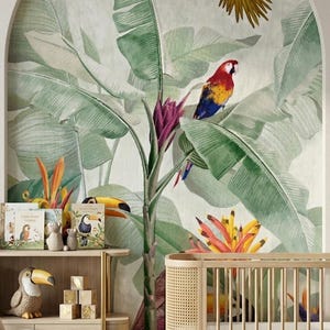 Op de afbeelding: Een kinderkamer met een tropisch thema. Een muurschildering van papegaaien en weelderig groen loof siert de muur. Een houten wieg, een boekenplank en een fauteuil bevinden zich in de kamer. Decoratieve toekanbeeldjes en kinderboeken worden tentoongesteld.