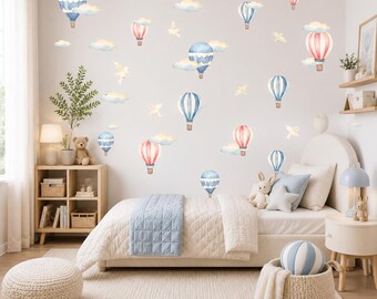 May include: A set of wall decals featuring watercolor-style hot air balloons in shades of blue, pink, and white, interspersed with clouds and small birds. The decals are applied to a plain wall above a bed with a light blue blanket and pillows.