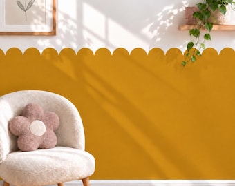 May include: A mustard yellow scalloped wall decal applied to the lower half of a white wall. A cream-colored textured armchair sits in front of the wall, featuring a plush, flower-shaped pillow in a muted mauve tone with a cream center.