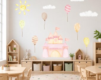 May include: A set of wall decals featuring a watercolor-style pink castle, a yellow sun, white clouds, and various patterned balloons in shades of pink, yellow, and beige. The designs are arranged on a wall above a wooden storage unit.