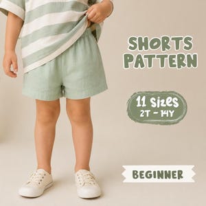 May include: Sage green shorts with an elastic waistband, paired with a matching sage and white striped shirt. Text on the image reads SHORTS PATTERN, 11 sizes 2T-14Y, and BEGINNER. The shorts are worn with white sneakers on a neutral background.