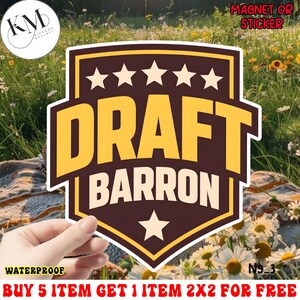 May include: A waterproof sticker or magnet featuring a shield design with the words "DRAFT BARRON" in bold yellow letters. The design includes five stars at the top and one at the bottom, all on a brown background.