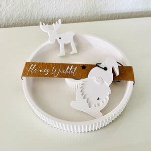 May include: White ceramic Christmas tree ornament featuring a white reindeer and gnome design. The ornament has a brown label that reads "Kleines Wichtel".