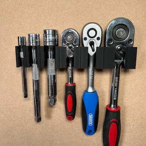 May include: A set of six chrome vanadium ratchets and extension bars hanging on a black wall-mounted organiser. The ratchets have black and red handles, and one has a blue handle with the word "DRAPER" printed on it.