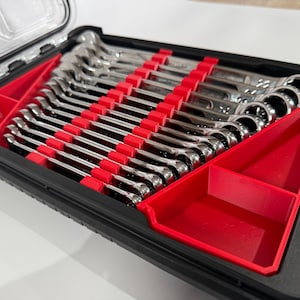 Puede incluir: Una caja de plástico negra con un interior rojo contiene un juego de llaves de tuercas. Las llaves están dispuestas en filas y todas son del mismo tamaño.