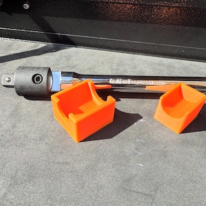 Könnte beinhalten: Ein orangefarbener Werkzeugorganizer mit zwei offenen Fächern befindet sich neben einem schwarz-silbernen Schraubenschlüssel. Der Schraubenschlüssel ist lang und hat einen schwarzen Kopf. Der Organizer besteht aus Kunststoff und ist leuchtend orange.