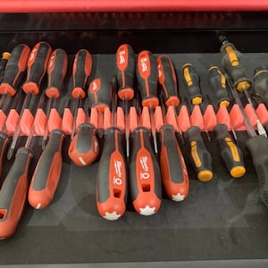 May include: A close-up of a toolbox drawer containing a selection of screwdrivers, neatly arranged in a red plastic holder. The screwdrivers are predominantly red and black, with some yellow accents.