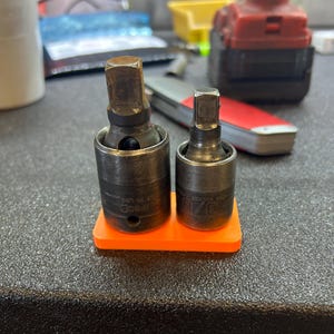 May include: Two black metal socket adapters with orange plastic holders. The larger adapter has the text "3/8" drive" and the smaller adapter has the text "1/4" drive".