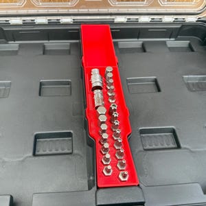 Könnte beinhalten: Eine schwarze Werkzeugkiste mit transparentem Deckel, die einen roten Organizer mit verschiedenen silbernen und grauen Metallbits enthält. Die Bits sind in verschiedenen Formen und Größen erhältlich und für die Verwendung mit einer Ratsche oder einem Schraubendreher konzipiert.