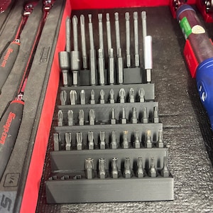 May include: A black plastic organizer with multiple rows of different sized screwdriver bits. The organizer is filled with a variety of screwdriver bits, including Phillips, flathead, and Torx.