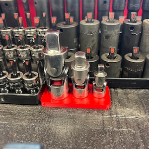 May include: Three silver socket adapters of different sizes on a red plastic holder. The adapters are used to connect different sizes of sockets to a wrench.