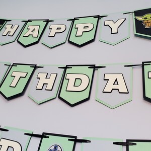 May include: A green and white banner with the words "Happy Birthday" and a cartoon character. The banner is made of paper and has black string attached to it.
